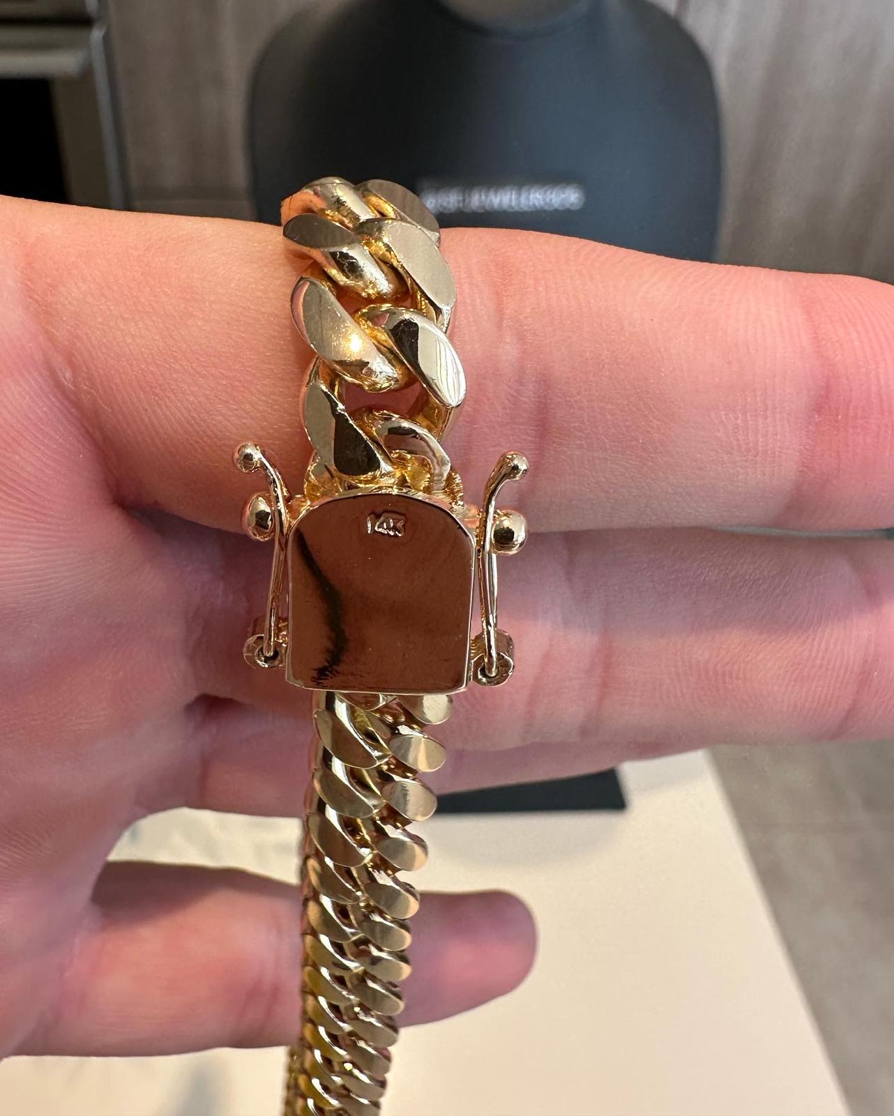 Man holding a 10MM  yellow gold over silver Cuban link chain, showing it stamped. The bold Miami Cuban chain has a heavy, polished finish and is styled with a casual t-shirt.