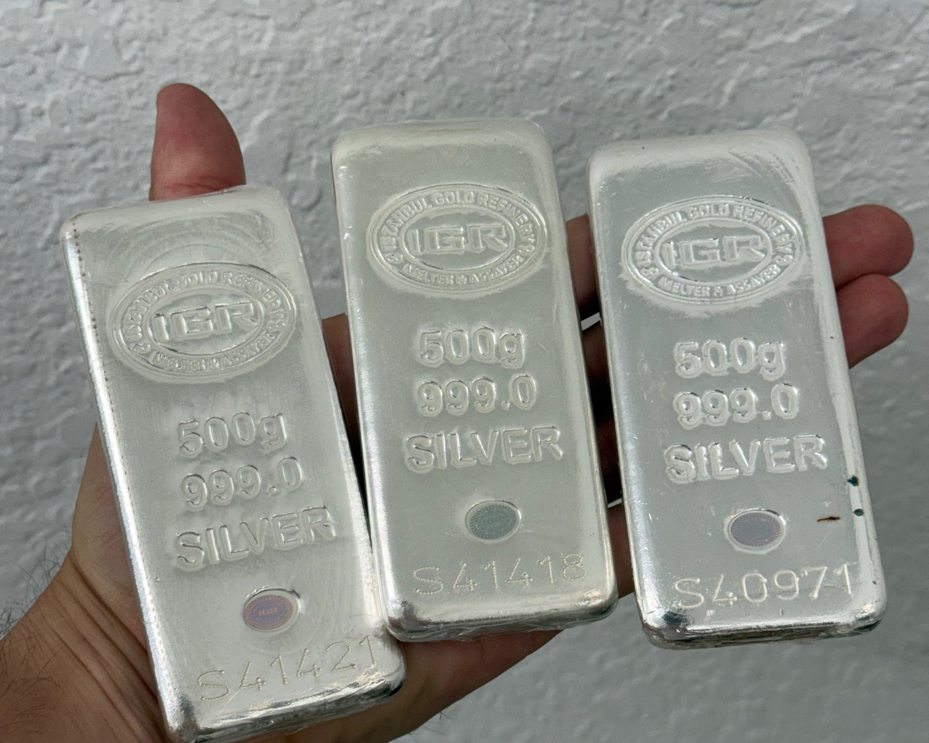 Three silver bars held in a hand against a plain background