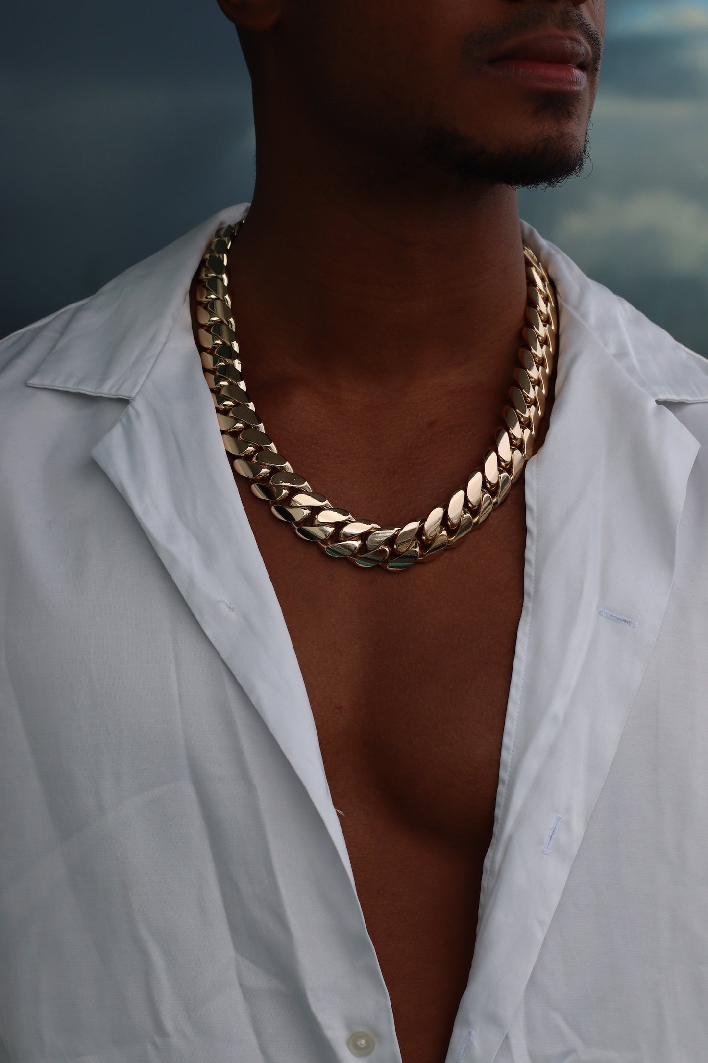 Man wearing a 20MM 24-inch yellow gold over silver Cuban link chain, modeled by SF Jeweler 305. The bold Miami Cuban chain has a heavy, polished finish and is styled with a casual t-shirt.
